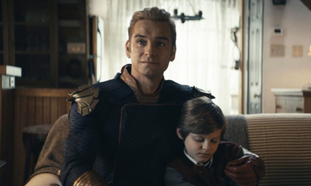 Homelander (Capitão Pátria) sentado ao lado de Ryan no sofá e o abraçando em cena do episódio 8 da 2ª temporada de The Boys.
